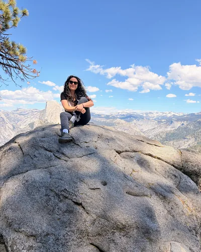 Lorena sitting on a granite dome high above a valley, with mountains to the horizon behind her.